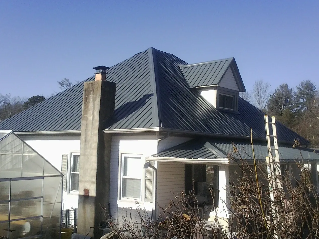 Dark blue standing seam metal roof on a white farmhouse with dormer — Slate & Tile Roof Repair by Roofing Brothers in North Lima