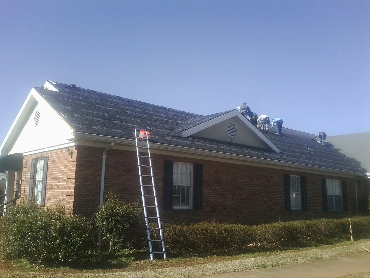 Crew tearing shingles off a brick ranch roof with a ladder set — Emergency Roof Repair work by our crew in North Lima