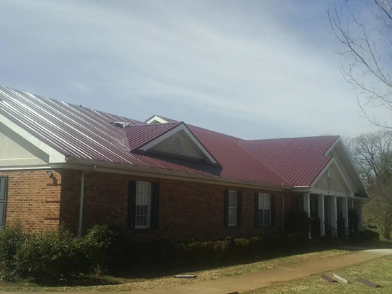 Red metal roof with gabled entries on a long brick building, from a Hail Damage Roof Repair job in North Lima