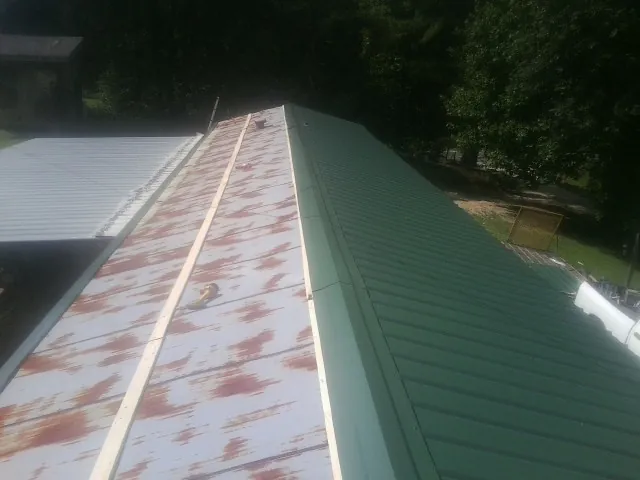 Old rusted panels beside newly installed green metal roofing — Wind Damage Roof Repair by Roofing Brothers in North Lima