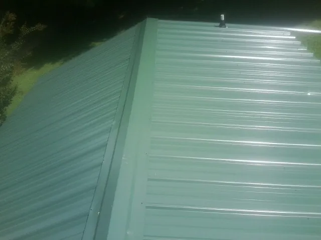 New green metal panels meeting at the ridge of a roof — Flat Roof Repair work by our crew in North Lima