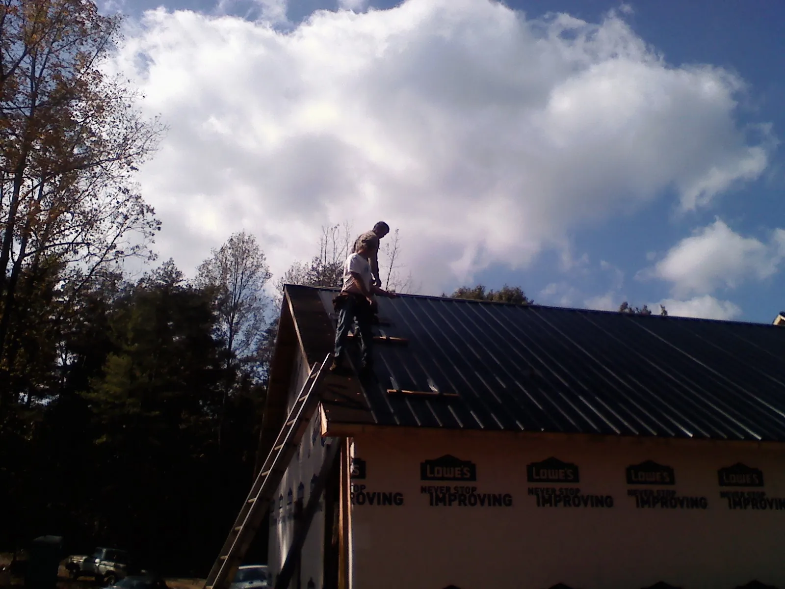 Roofer fastening dark metal panels high against a cloudy sky, from a Roof Inspection job in North Lima