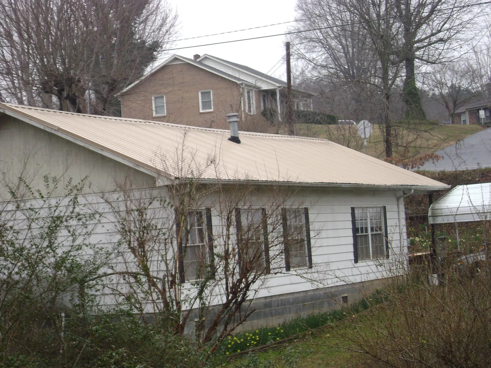 Tan metal roof on a white sided house set into a hillside — Commercial Roofing by Roofing Brothers in North Lima